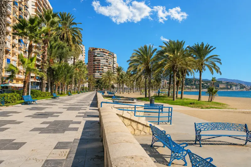 Paseo Marítimo Ciudad de Melilla junto a la playa de La Malagueta, con palmeras, bancos azules y vistas al mar en Málaga