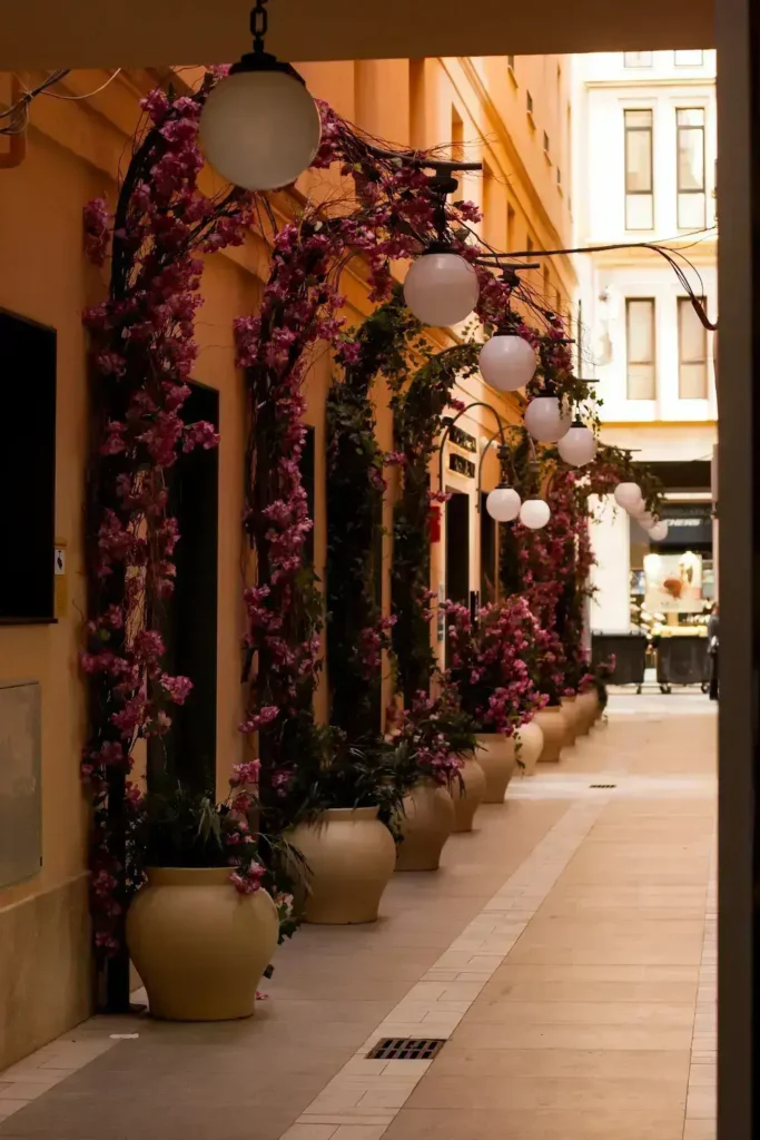 Pasaje interior decorado con buganvillas rosas, macetas y lámparas colgantes en el centro de Málaga